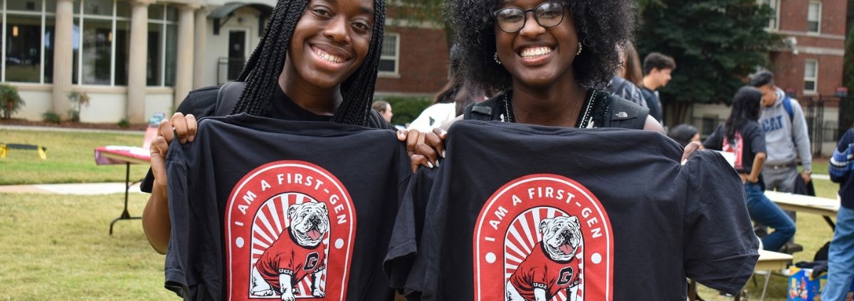 Two smiling students holding t-shirts that say "I am a first-gen Bulldog"