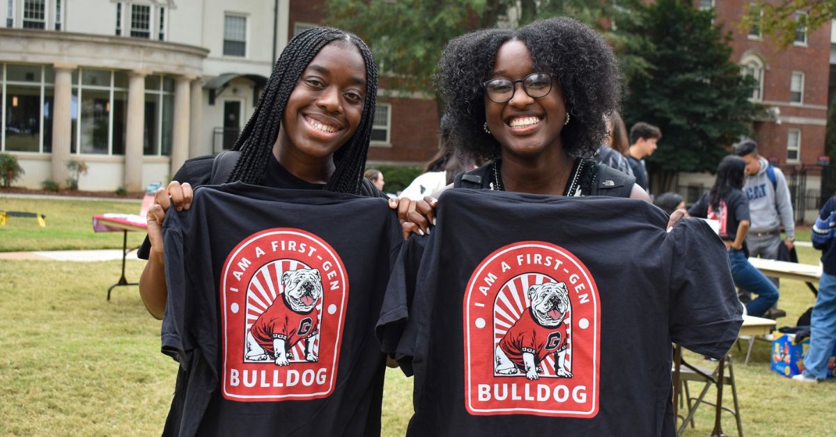 Two smiling students holding t-shirts that say "I am a first-gen Bulldog"