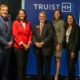 A group of people stand smiling in front of a Truist sign.