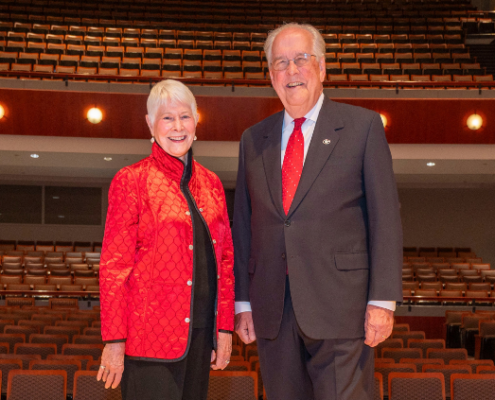 A smiling man and woman stand on a stage in a concert hall.