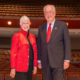 A smiling man and woman stand on a stage in a concert hall.