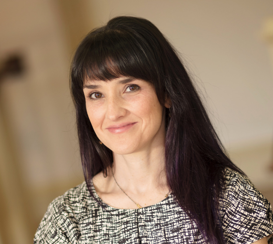 A closeup photo of a smiling woman in front of a beige background. 