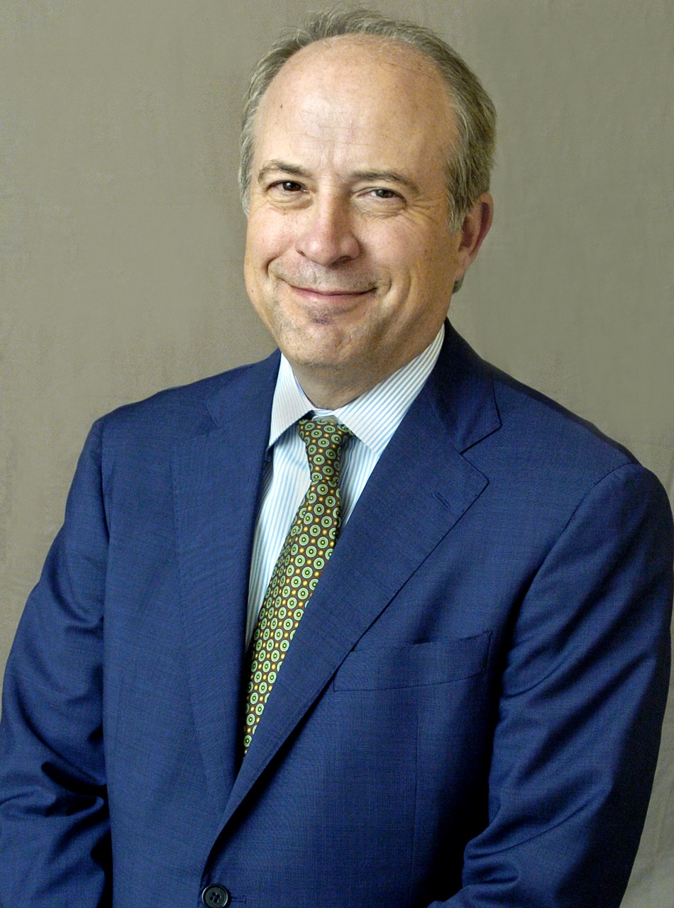 A close-up of a smiling man in front of a grey background. 