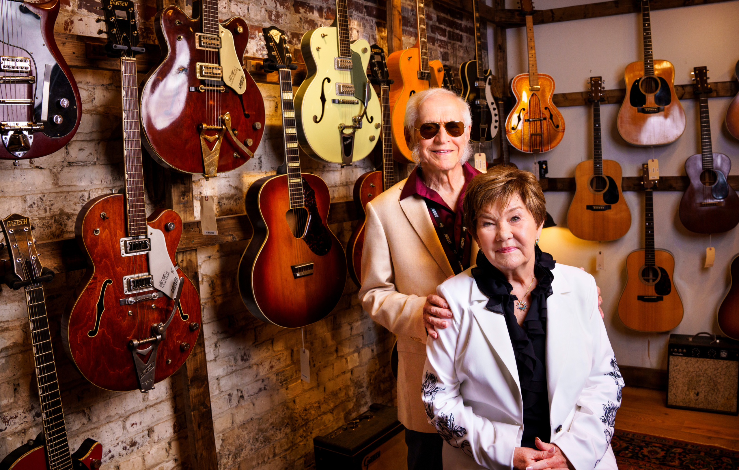 Fred and Dinah Gretsch pictured in front of a wall of vintage guitars, some including Gretsch guitars, in Athens. 