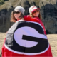 Two smiling students wrapped in red University of Georgia flag on top of mountain.
