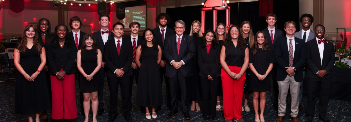 A group of smiling students and President Morehead standing in a ballroom.