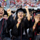 Excited students in graduation gowns at commencement.