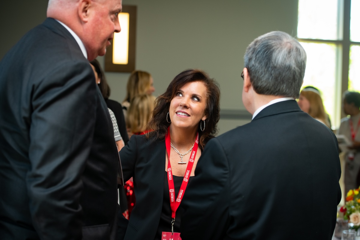 GWG2-279 A woman in a red lanyard talks with two men in dark suits at an event.