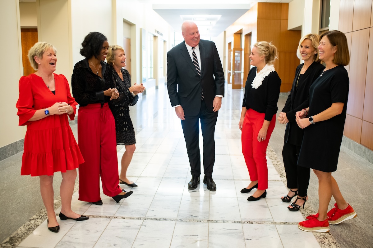 GWG2-37 Six people laugh together in a hallway, with a man in a dark suit at center.