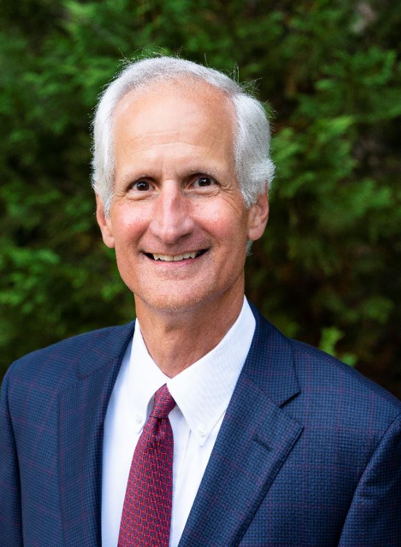 A man smiles in front of green foliage. 