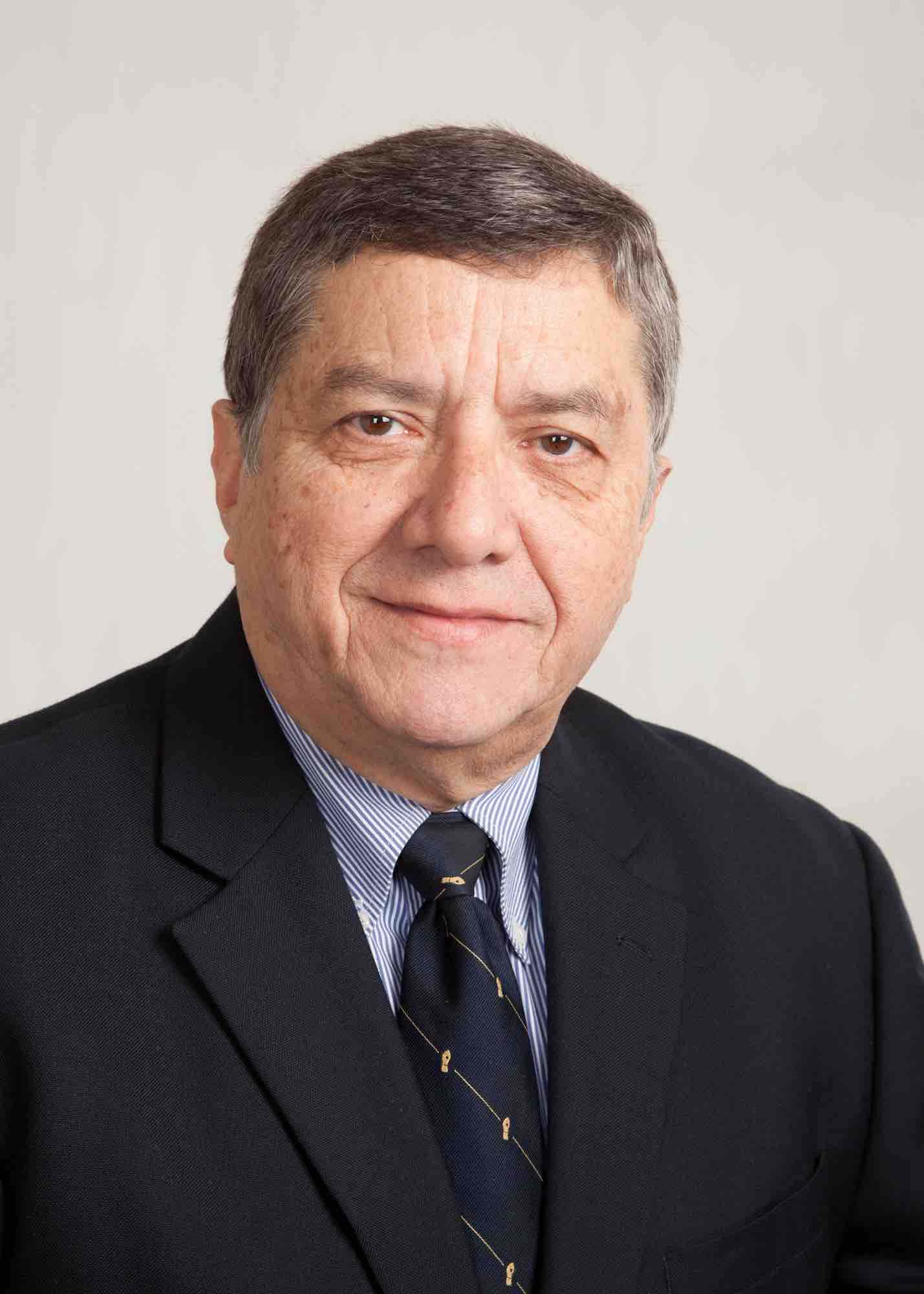 A closeup headshot of a man in front of a grey background. 