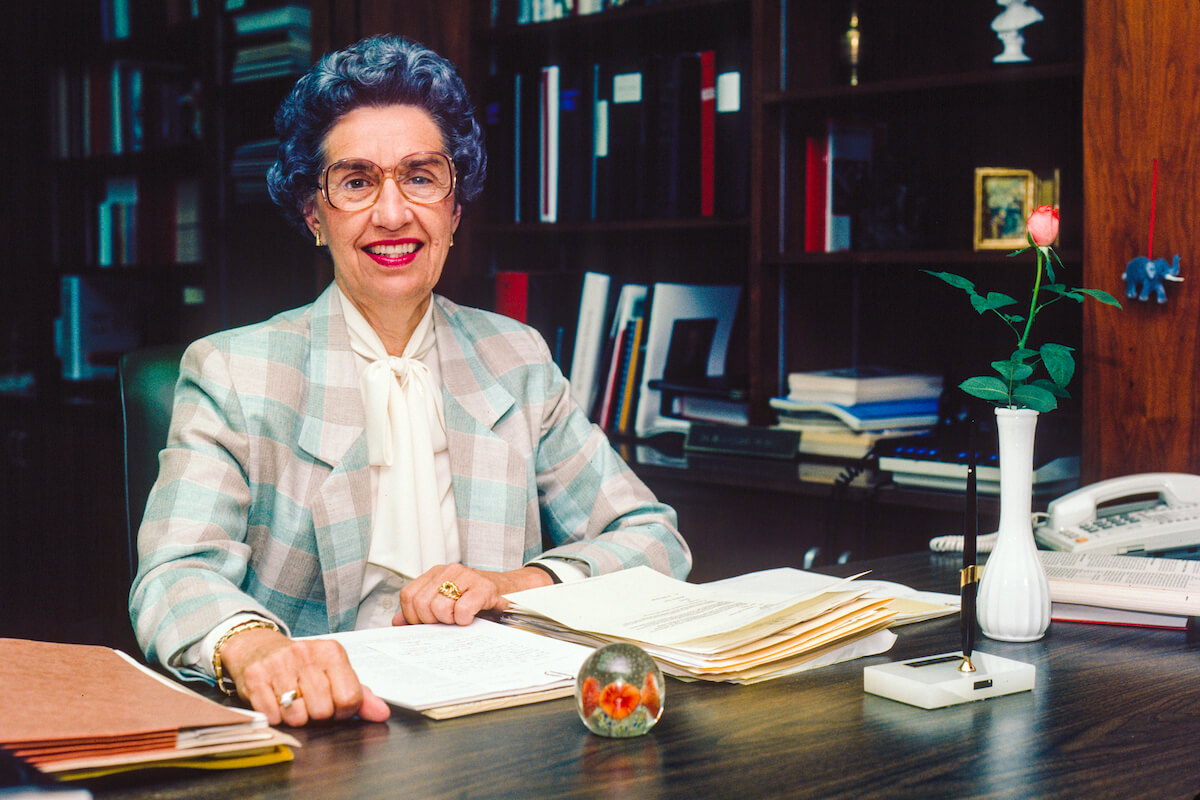 McBee-2023-GWGsiteflip-V1 Louise McBee smiling at her office desk covered in papers.