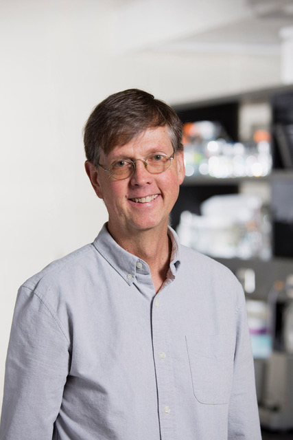 A closeup photo of a smiling man standing in a laboratory setting.