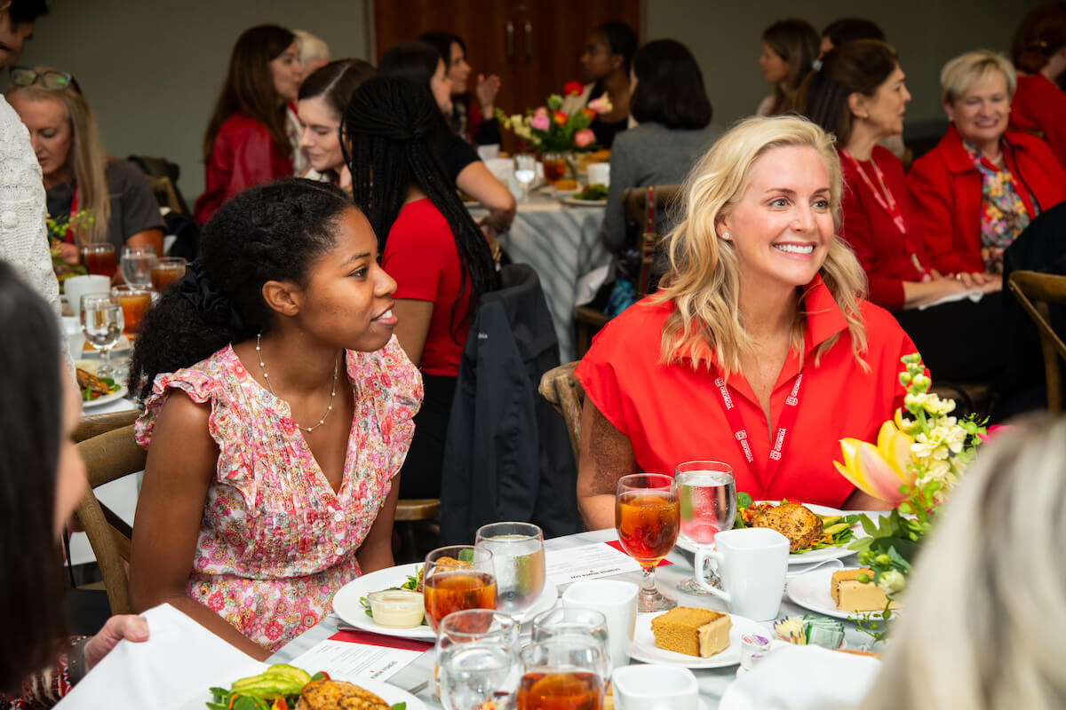 Student-2024-GWGWebUpdates-V1 Two women smile and chat at a luncheon table set with red drinks and cake slices.