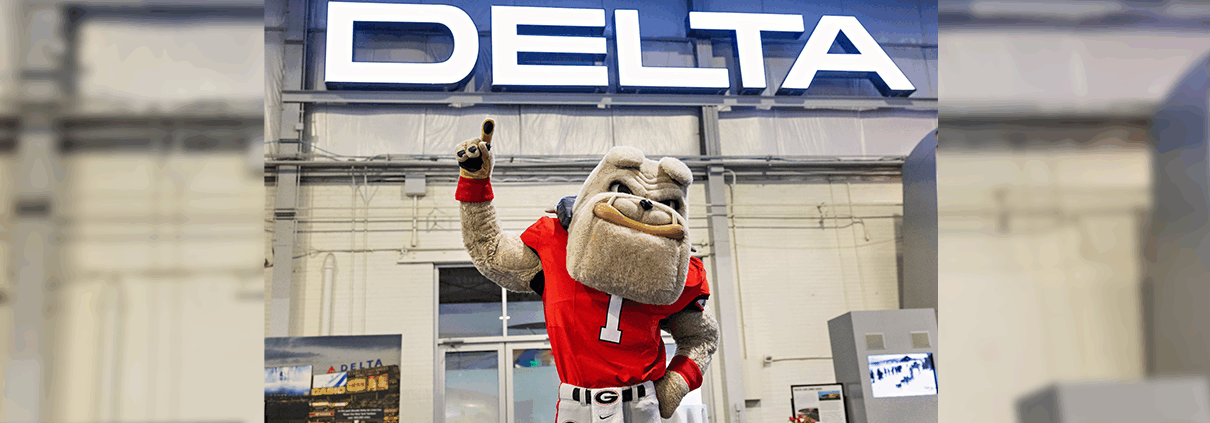 UGA mascot, Hairy Dawg, poses in front of a Delta sign.