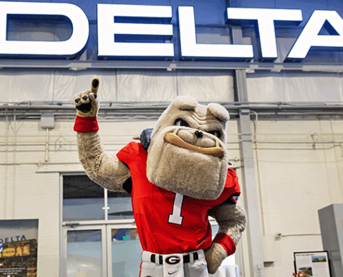 UGA mascot, Hairy Dawg, poses in front of a Delta sign.