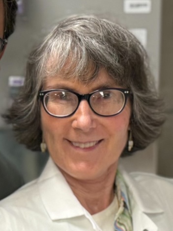 A close-up headshot of a smiling woman with black rimmed glasses.